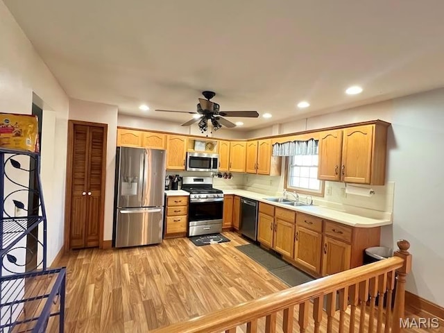 kitchen featuring appliances with stainless steel finishes, a sink, light wood finished floors, light countertops, and baseboards