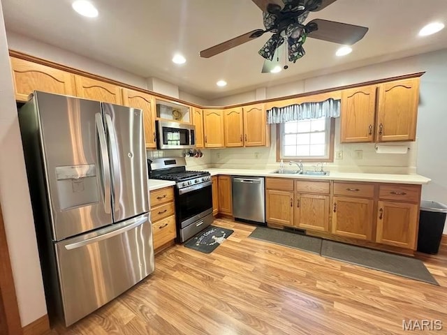 kitchen featuring stainless steel appliances, a sink, light wood-type flooring, light countertops, and ceiling fan