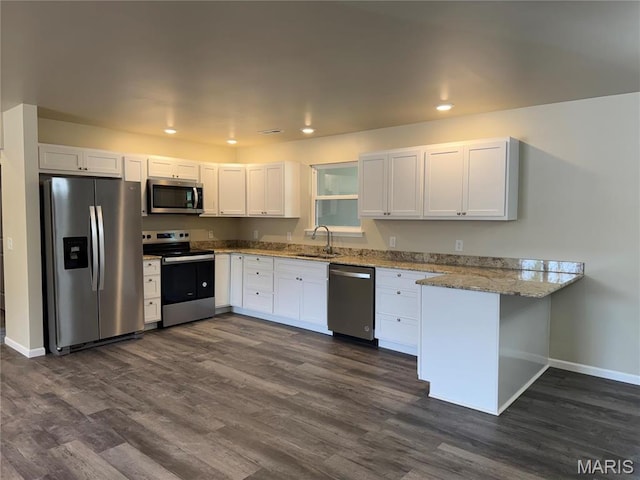 kitchen featuring appliances with stainless steel finishes, a peninsula, a sink, baseboards, and light stone counters