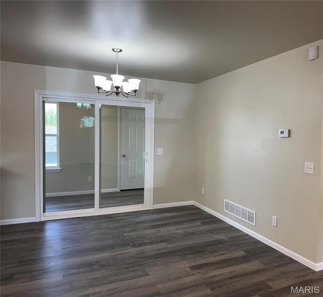 empty room featuring a chandelier, dark wood-type flooring, and baseboards