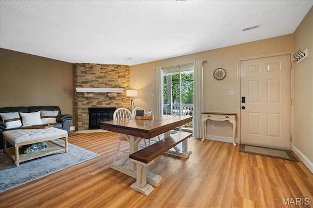 9005 Cardinal Ter, Saint Louis, MO 63144 - dining space featuring light wood finished floors, a stone fireplace, a textured ceiling, and baseboards