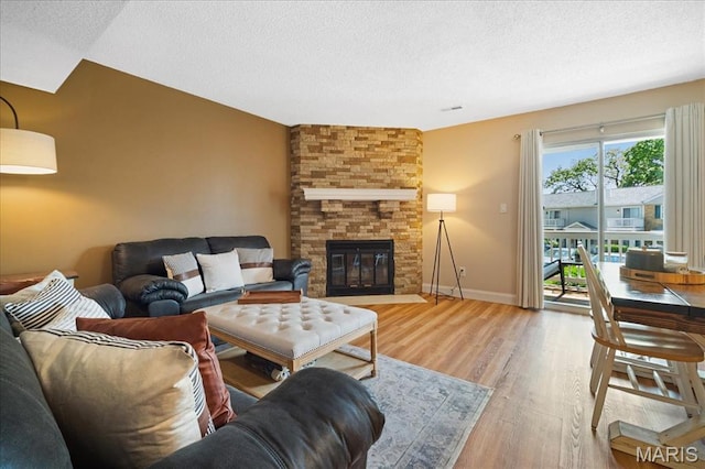 9005 Cardinal Ter, Saint Louis, MO 63144 - living room featuring wood finished floors, a textured ceiling, a stone fireplace, and baseboards