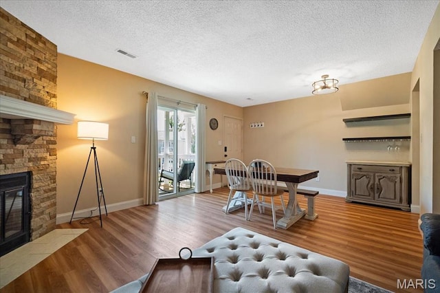 9005 Cardinal Ter, Saint Louis, MO 63144 - dining room with a textured ceiling, wood finished floors, a stone fireplace, and baseboards