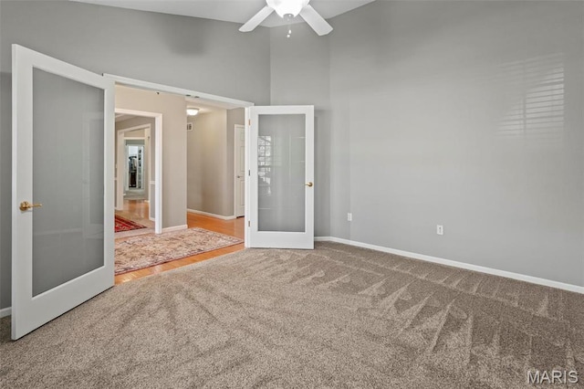 unfurnished bedroom with french doors, carpet flooring, baseboards, and a towering ceiling