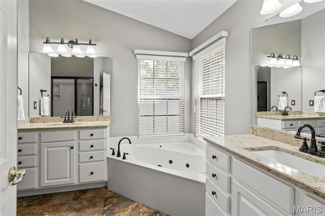 full bath featuring vaulted ceiling, stone finish flooring, a tub with jets, and two vanities