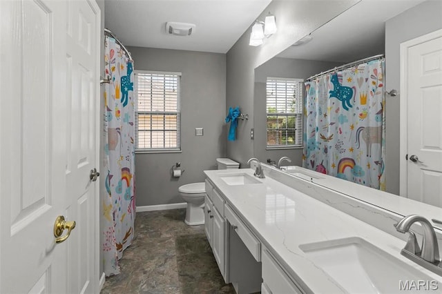 full bathroom featuring baseboards, stone finish flooring, toilet, and double vanity