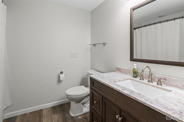 bathroom featuring wood finished floors, baseboards, vanity, and toilet