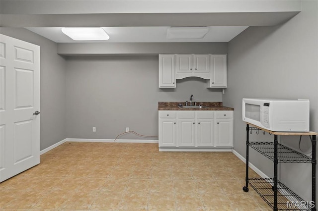 kitchen with white microwave, white cabinetry, a sink, dark countertops, and light tile patterned floors