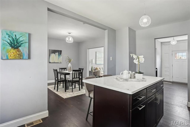 5327 W Ave, Saint Louis, MO 63116 - kitchen featuring dark wood-type flooring, baseboards, a breakfast bar area, and hanging light fixtures