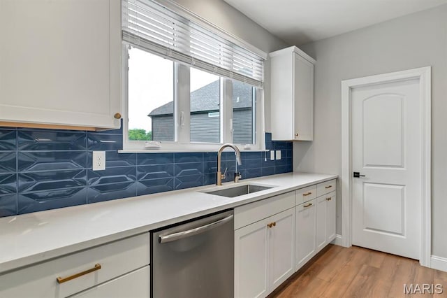 kitchen with dishwasher, a sink, tasteful backsplash, white cabinetry, and light wood finished floors
