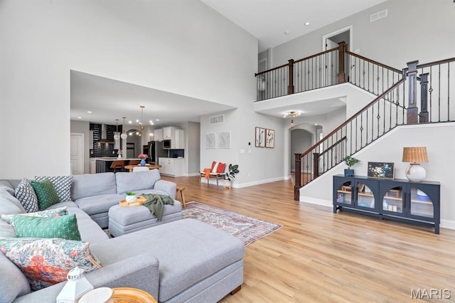 living area featuring light wood finished floors, stairs, a towering ceiling, arched walkways, and a chandelier