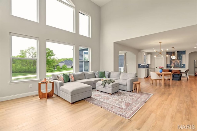 215 Everett Creek Ct, Lake St Louis, MO 63367 - living room with arched walkways, a chandelier, light wood finished floors, baseboards, and a towering ceiling
