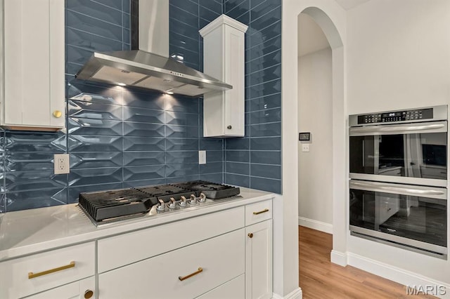 215 Everett Creek Ct, Lake St Louis, MO 63367 - kitchen with appliances with stainless steel finishes, wall chimney exhaust hood, decorative backsplash, white cabinetry, and arched walkways