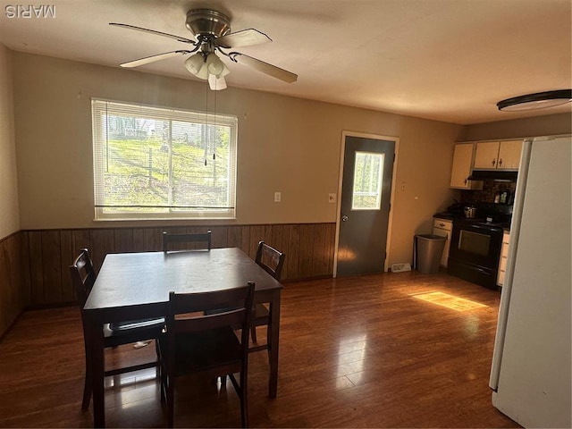 dining area featuring a wainscoted wall, wooden walls, healthy amount of natural light, a ceiling fan, and wood finished floors
