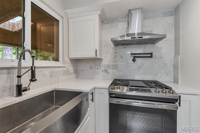 kitchen featuring gas stove, wall chimney range hood, a sink, tasteful backsplash, and white cabinetry