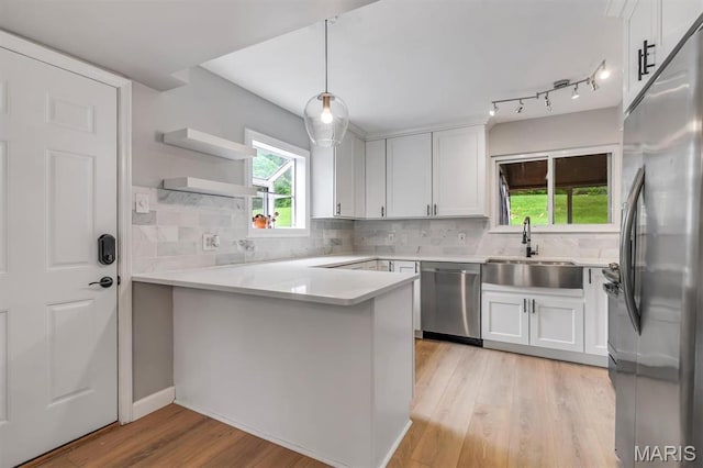 kitchen with stainless steel appliances, a sink, a peninsula, light wood-style flooring, and white cabinetry