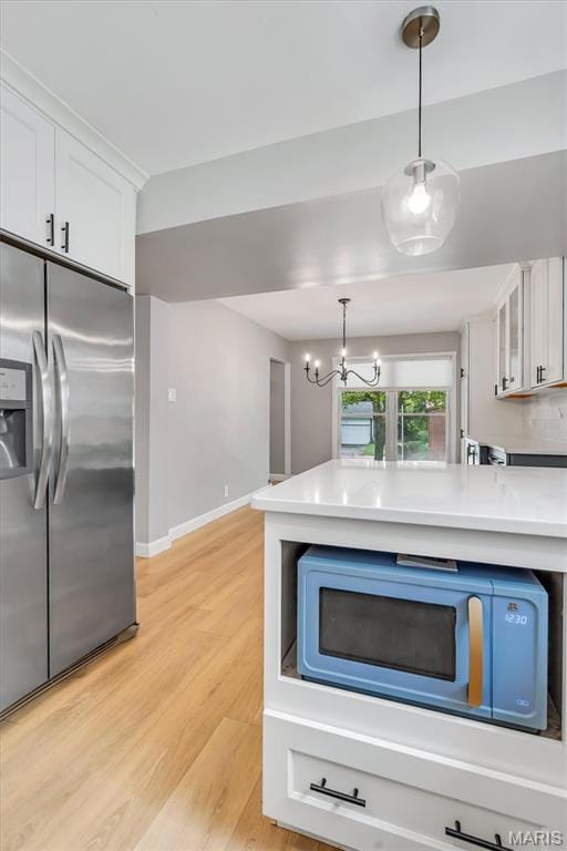 kitchen with stainless steel fridge, white microwave, white cabinets, light wood-type flooring, and hanging light fixtures
