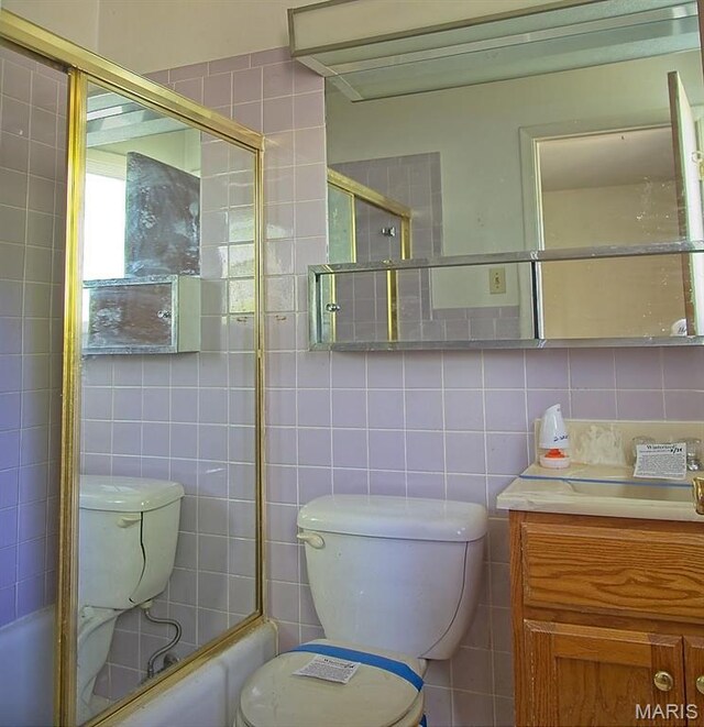 bathroom featuring tile walls, toilet, vanity, and bath / shower combo with glass door