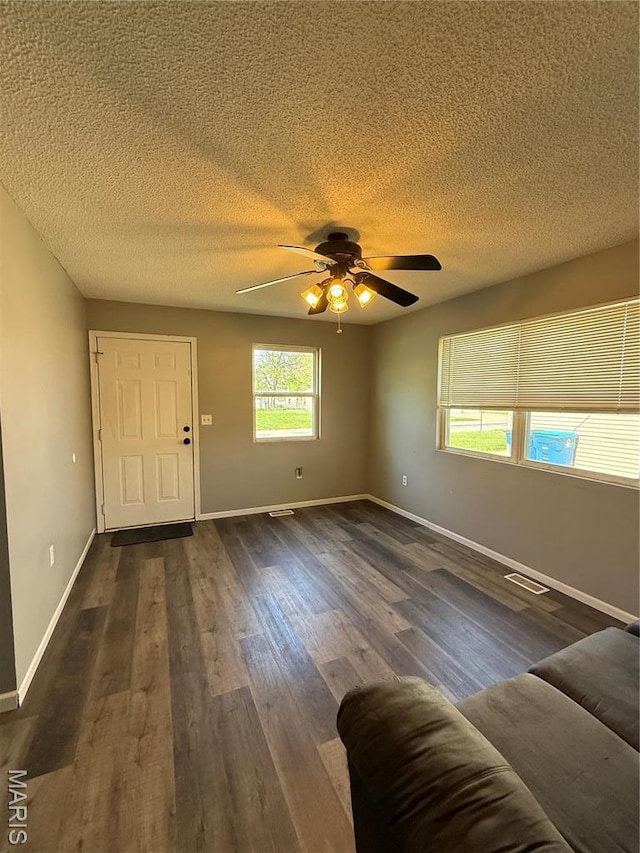 unfurnished living room with dark wood finished floors, ceiling fan, a textured ceiling, and baseboards