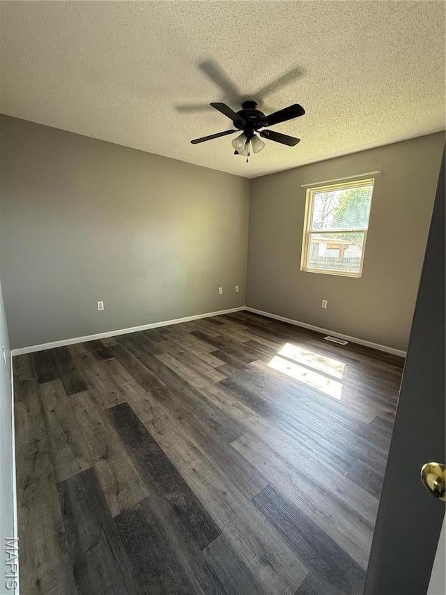 spare room with a textured ceiling, a ceiling fan, dark wood finished floors, and baseboards