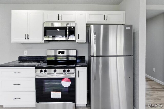 619 E 3rd St, De Soto, MO 63020 - kitchen featuring stainless steel appliances, light wood-type flooring, white cabinets, baseboards, and dark stone countertops