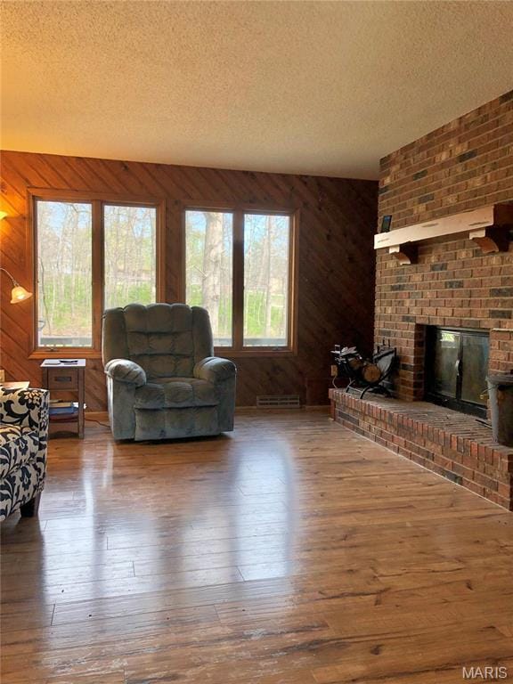 10280 County Road 3110, Rolla, MO 65401 - living room featuring a brick fireplace, plenty of natural light, hardwood / wood-style floors, a textured ceiling, and wood walls