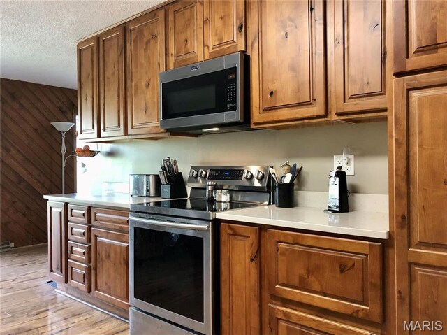 10280 County Road 3110, Rolla, MO 65401 - kitchen featuring appliances with stainless steel finishes, light wood-style flooring, brown cabinets, wood walls, and light countertops