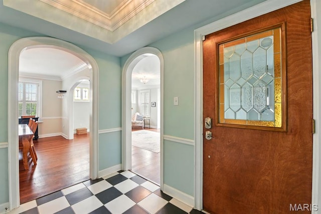 foyer featuring tile patterned floors, arched walkways, baseboards, and ornamental molding