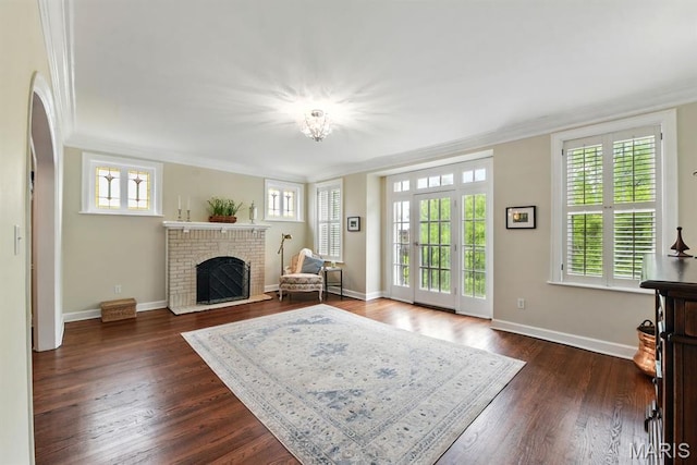 living room featuring ornamental molding, dark wood finished floors, a brick fireplace, arched walkways, and baseboards