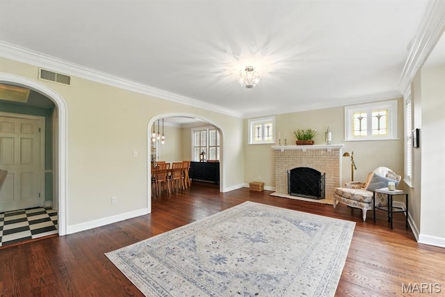 living room with arched walkways, a chandelier, ornamental molding, wood finished floors, and a brick fireplace