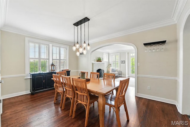 dining room featuring arched walkways, healthy amount of natural light, dark wood-style floors, ornamental molding, and a brick fireplace