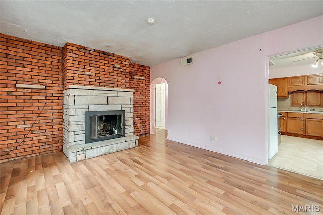 225 Whitelaw Ave, East Alton, IL 62024 - unfurnished living room with light wood-type flooring, a fireplace, a sink, arched walkways, and brick wall