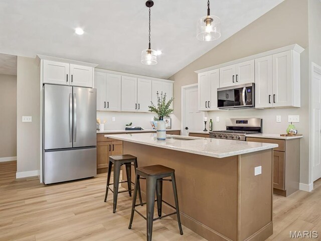 kitchen with stainless steel appliances, light wood-style floors, a kitchen island with sink, hanging light fixtures, and a breakfast bar