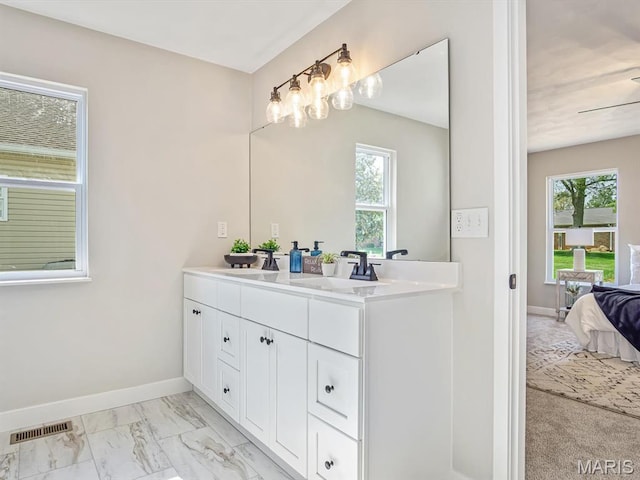 ensuite bathroom with plenty of natural light, double vanity, baseboards, and marble finish floors