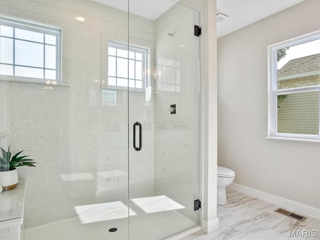 bathroom with healthy amount of natural light, toilet, baseboards, and a stall shower