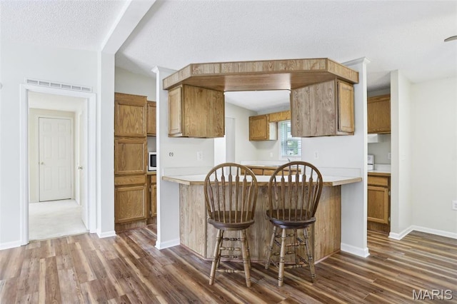 21839 Dove Ln, Carlyle, IL 62231 - kitchen featuring dark wood-style flooring, brown cabinets, light countertops, white microwave, and a breakfast bar