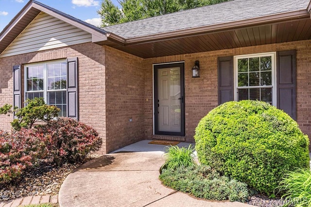 property entrance with brick siding, a shingled roof, and covered porch