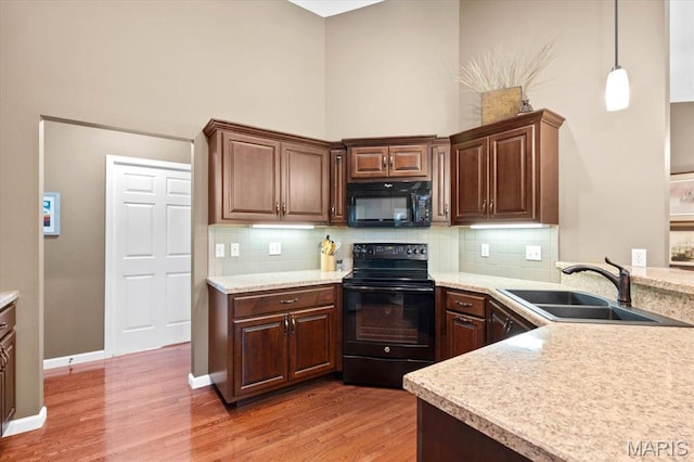 kitchen featuring black appliances, a sink, light wood-type flooring, light countertops, and backsplash