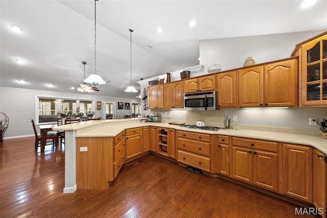 kitchen featuring stainless steel microwave, a peninsula, glass insert cabinets, hanging light fixtures, and light countertops