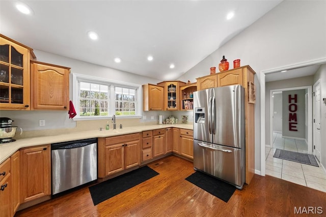 kitchen with appliances with stainless steel finishes, a sink, glass insert cabinets, lofted ceiling, and light countertops