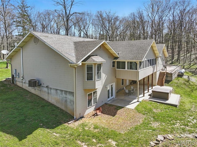 rear view of house featuring roof with shingles, a patio, cooling unit, a yard, and a sunroom