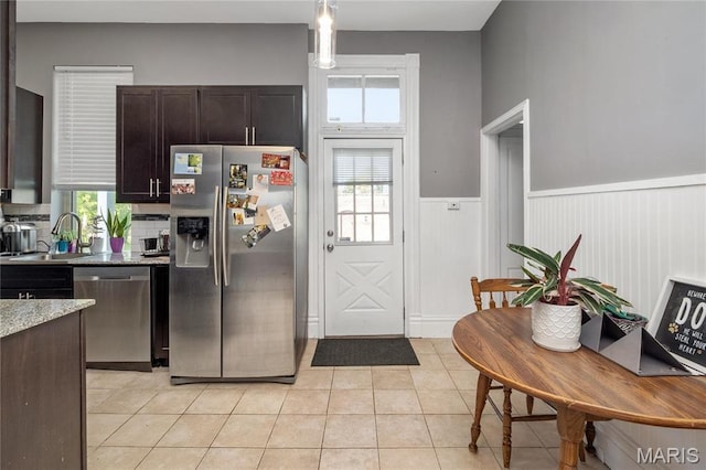 kitchen with stainless steel appliances, a sink, wainscoting, dark brown cabinetry, and light tile patterned flooring