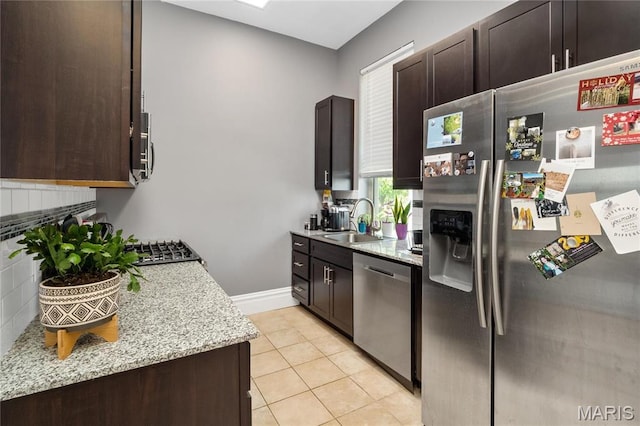 kitchen with appliances with stainless steel finishes, a sink, dark brown cabinetry, decorative backsplash, and light stone countertops