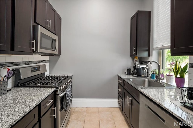 kitchen featuring stainless steel appliances, a sink, decorative backsplash, baseboards, and light stone counters