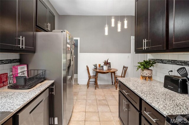 kitchen featuring decorative backsplash, light stone counters, wainscoting, light tile patterned flooring, and dark brown cabinets