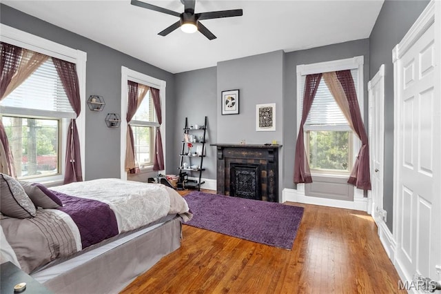 bedroom featuring wood finished floors, a fireplace, baseboards, and a ceiling fan