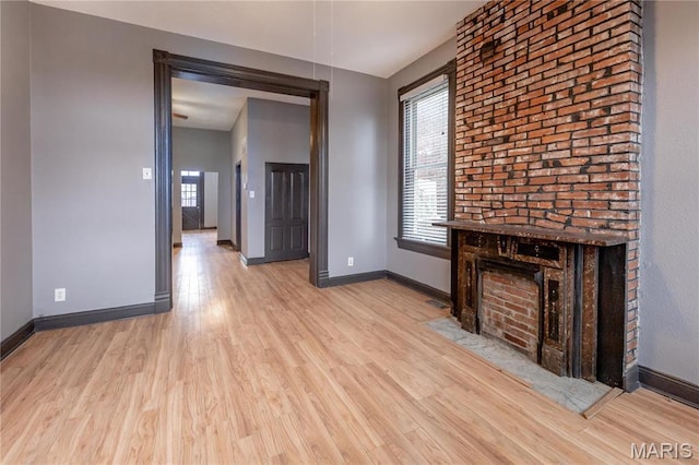 unfurnished living room with healthy amount of natural light, light wood finished floors, baseboards, and a fireplace