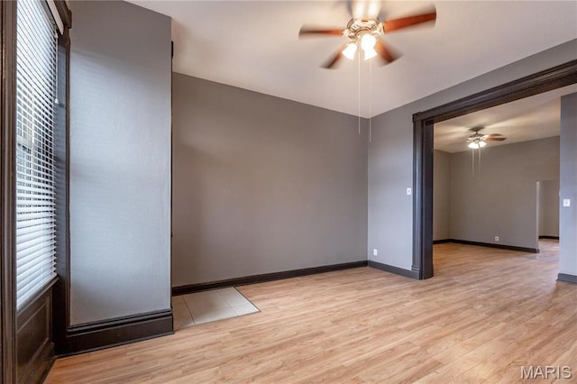 spare room with a ceiling fan, light wood-type flooring, and baseboards