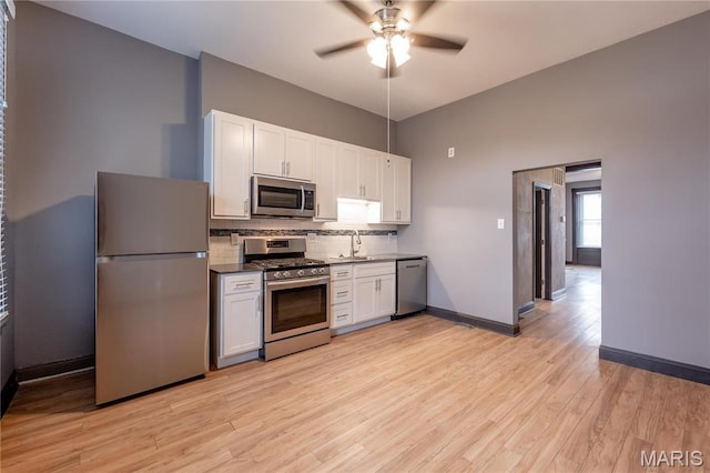kitchen with stainless steel appliances, ceiling fan, backsplash, light wood-style floors, and white cabinetry