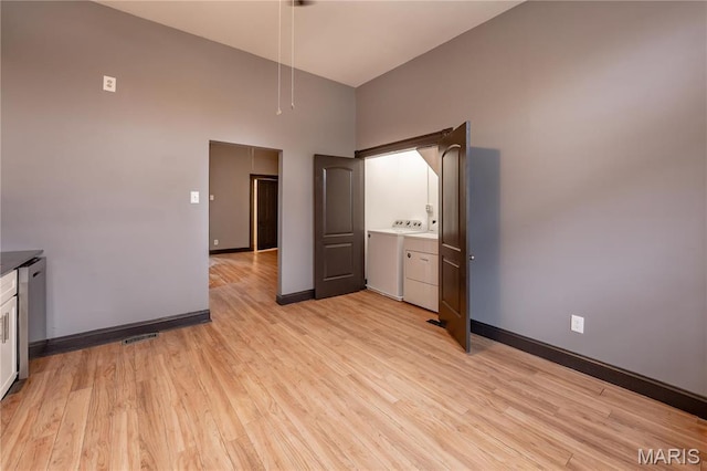 empty room with a high ceiling, washing machine and dryer, light wood-style floors, and baseboards